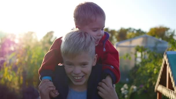 Niño abrazando a su hermano menor y lo sostiene sobre sus hombros. Risa y alegría de los niños. Puesta de sol — Vídeo de stock