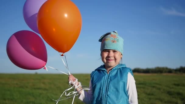 Милая девушка, стоящая с воздушными шарами в поле — стоковое видео