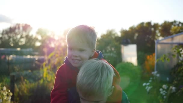 Niño abrazando a su hermano menor y lo sostiene sobre sus hombros. Risa y alegría de los niños. Puesta de sol — Vídeos de Stock