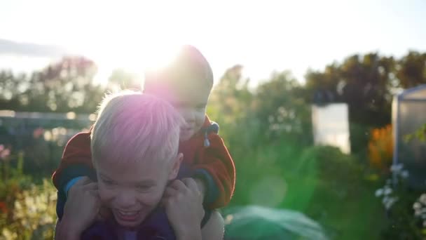 Junge umarmt seinen jüngeren Bruder und hält ihn auf seinen Schultern. Kinderlachen und -freude. Sonnenuntergang — Stockvideo