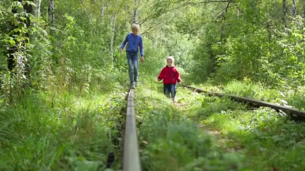 Een eenzame tiener jongen en zijn jongere broer lopen op de trein sporen — Stockvideo