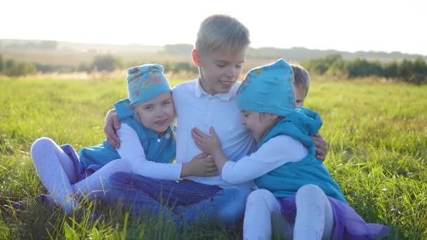 Los niños se sientan en el césped del parque. Ríanse, abracen y sonrían. Vacaciones infantiles al aire libre — Vídeos de Stock