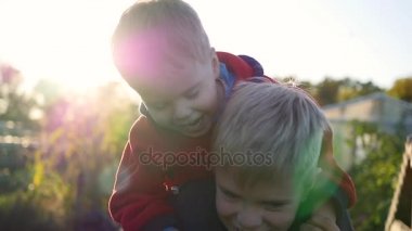 Çocuk küçük kardeşi sarılma ve ona onun omuzlarında tutar. Çocuk kahkaha ve neşe. Günbatımı