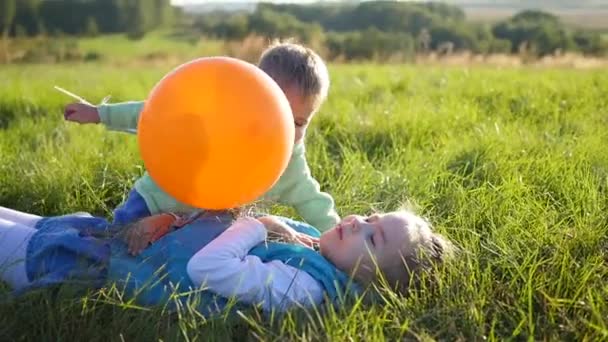Счастливые дети играют в парке. Мальчик обнимает и целует свою сестру. Воздушный шар. Смех и улыбки детей — стоковое видео