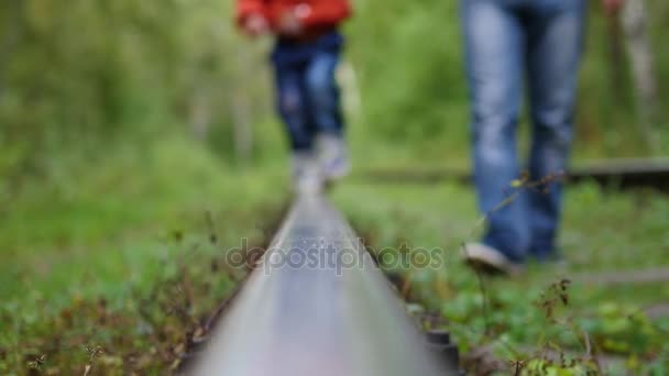 Primer plano. Las piernas están en las vías del tren. El tipo sostiene a un niño caminando por el ferrocarril — Vídeo de stock