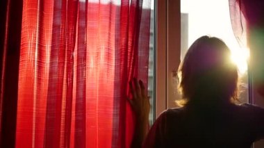 Kız kırmızı perdeler açılır ve elleri ile güneş ışınları ile oynadı. bir kız silüeti