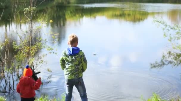 Τα παιδιά στέκονται στην όχθη της λίμνης και πετάνε πέτρες. Περίπατοι στον καθαρό αέρα — Αρχείο Βίντεο