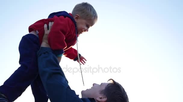 Медленное движение. Молодой отец подбрасывает своего смеющегося ребенка в воздух. Открытый отдых на природе — стоковое видео