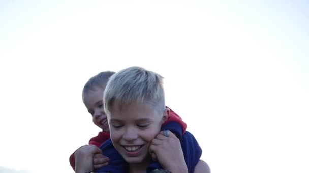 Niño abrazando a su hermano menor y lo sostiene sobre sus hombros. Risa y alegría de los niños. Puesta de sol — Vídeos de Stock