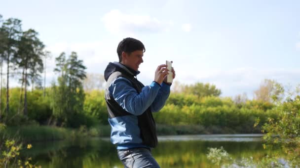 Молодой парень фотографирует осенний пейзаж по телефону . — стоковое видео