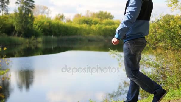 En kille kom fram till sjön och höjer händerna. Promenad i friska luften — Stockvideo