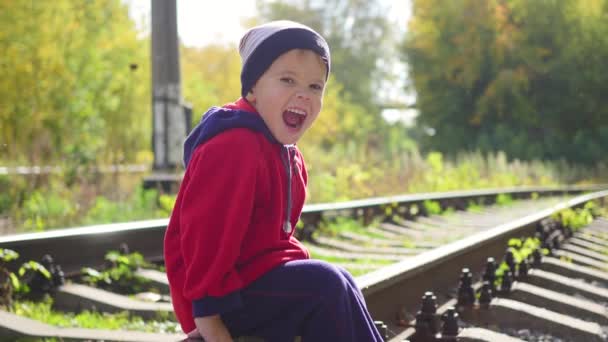 En ensam pojke sitter på järnvägsspåren. Farligt spel och underhållning — Stockvideo