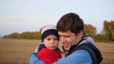 Genç bir baba çocuğunu onun kollarında tutar. Hassasiyet ve sevgili babam benimsemesi. Açık hava etkinlikleri