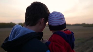 Genç çocuğunu ellerinde tutan baba ve gün batımını izlemek. Hassasiyet ve sevgili babam benimsemesi. Açık hava etkinlikleri
