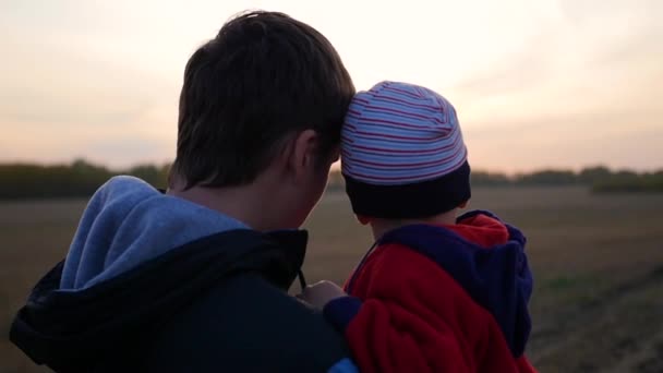 Mladý otec drží své dítě na rukou a sledovat západ slunce. Něha a objetí milovaného otce. Outdoorové aktivity — Stock video