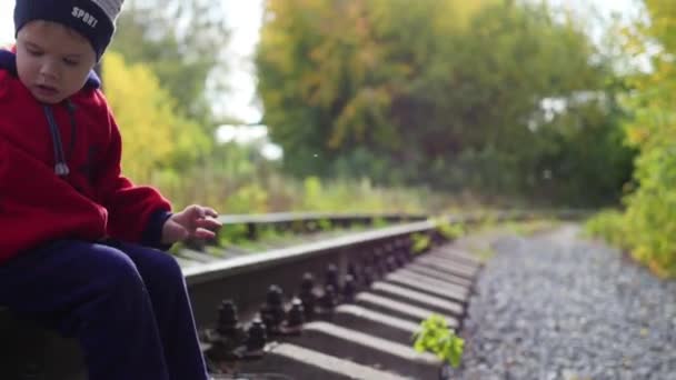 Ein einsamer Junge sitzt auf den Bahngleisen. Gefährliche Spiele und Unterhaltung — Stockvideo