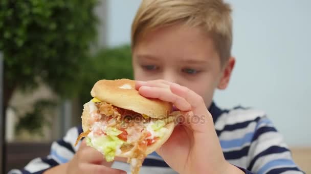 Ребенок ест булочку с курицей, сыром и зеленью в ресторане быстрого питания — стоковое видео