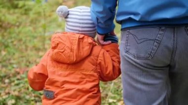Genç bir baba ile çocuk parkta yürüyor. Baba oğlu elini tutuyor. Hassasiyet ve sevgili babası sarılma.