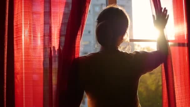 A lány vörös függönyök megnyílik, és játszott keresztül a napok sugarak a kezével. sziluettje egy lány — Stock videók