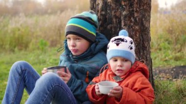 çim ve İçecek sıcak çay üzerinde oturan sonbahar Park çocuklarda temiz havada yürüyüş