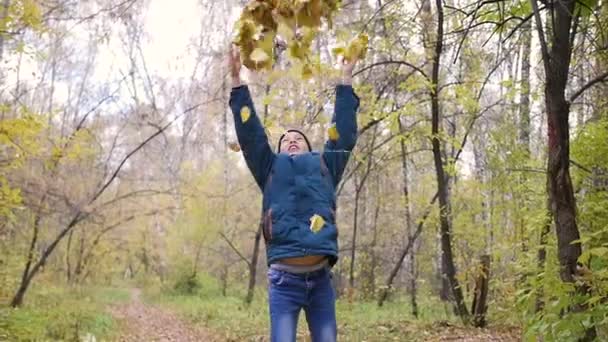 Un adolescent vomit des feuilles jaunes au-dessus de lui. Une promenade dans la forêt de pins 