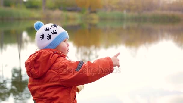 Un niño se para en la orilla del estanque y tira piedras. Caminatas al aire libre — Vídeos de Stock