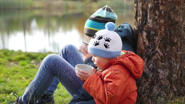 En el parque de otoño los niños sentados en el césped y beber té caliente, caminar al aire libre — Vídeos de Stock