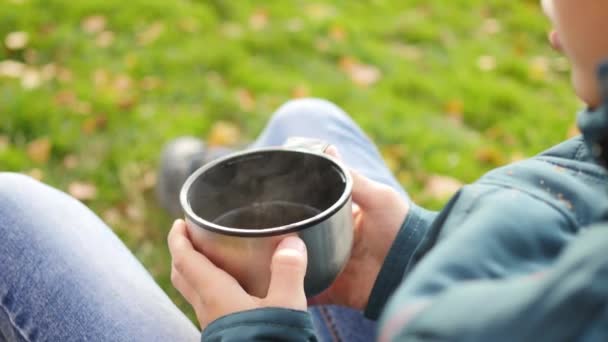 Őszi Park srác ül a gyep és italt forró tea séta a friss levegőn. Közeli kép a kezek — Stock videók