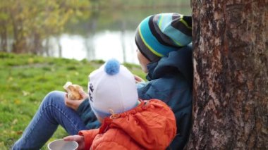 çim ve İçecek sıcak çay üzerinde oturan sonbahar Park çocuklarda temiz havada yürüyüş
