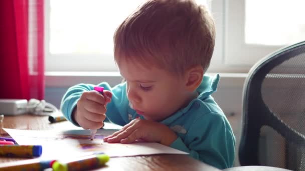 Çocuk heyecanla bir kağıt parçası üzerinde boya kalemi ile çizer. Okul öncesi eğitim — Stok video