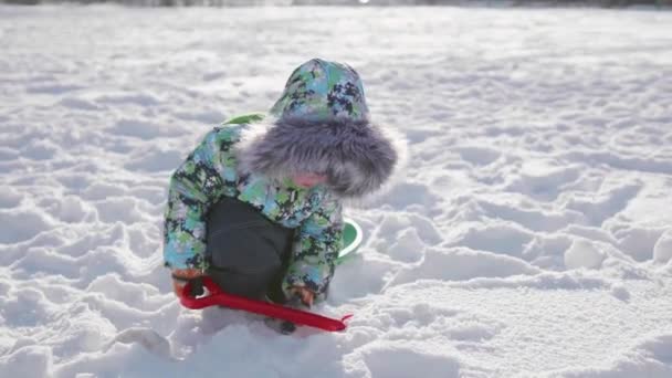 Egy kisgyermek játszik a hó a téli Park. Napos tél nap. Szórakozás és játékok a friss levegő. — Stock videók