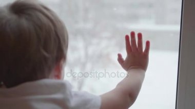 Bir pencere ve izlerken kar sokakta düşen yakınındaki bir çocuk duruyor. Cam pencere portre yandan