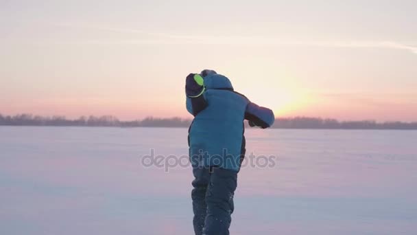 Een kind speelt in de winter buiten loopt, sneeuw gooit naar de top. Prachtige zonsondergang. Actieve outdoor sporten — Stockvideo