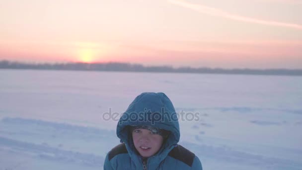 Uma criança brinca no inverno ao ar livre, corre, joga neve para o topo. Belo pôr-do-sol. Esportes ativos ao ar livre — Vídeo de Stock