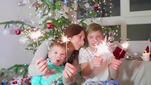 Šťastná rodina zapálil prskavky na večírku. V pozadí, bokeh světla a girlandy vánoční jedle — Stock video