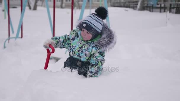 Ett litet barn som leker med snö i Vinterparken. Barnet håller en spade, massor av snö i parken. Kul och spel i friska luften. — Stockvideo