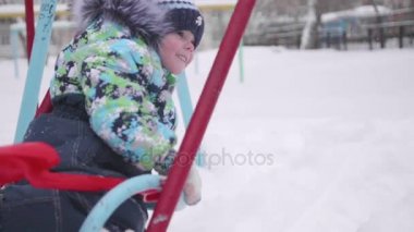 Küçük bir çocuk kış parkta oynuyor. Bir çocuk bir salıncak üzerinde. Güneşli kış günü. Eğlence ve oyun temiz havada.