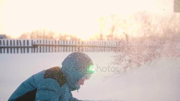 Un niño juega en el invierno al aire libre, lanza nieve a la cima. Deportes activos al aire libre. Puesta de sol — Vídeos de Stock