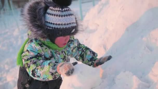 Un niño pequeño está jugando en un parque de invierno con nieve. Un día soleado de invierno. Diversión y juegos al aire libre . — Vídeo de stock