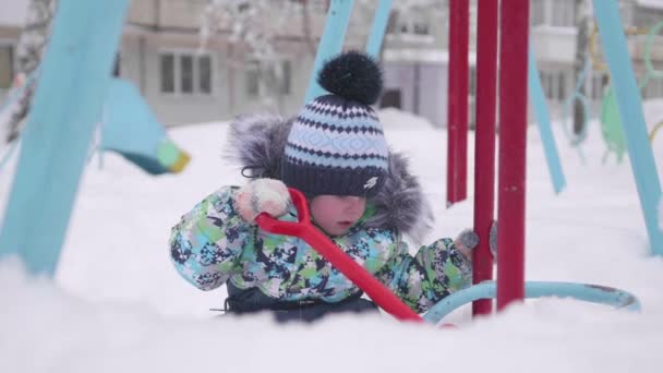 Un niño jugando con nieve en el parque de invierno. Niño sosteniendo una pala, mucha nieve en el parque. Diversión y juegos al aire libre . — Vídeo de stock