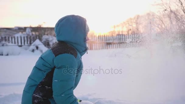 Uma criança brinca no inverno ao ar livre, joga neve para o topo. Esportes ativos ao ar livre. Pôr do sol — Vídeo de Stock