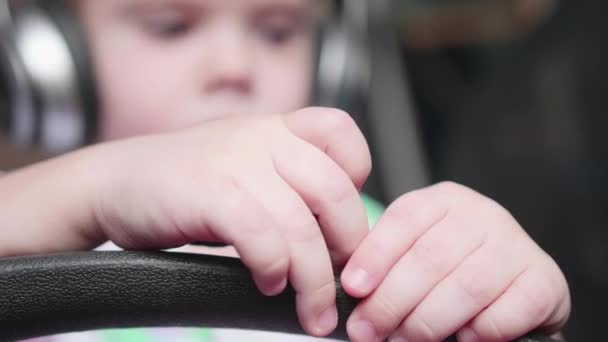 Un niño gracioso se sienta en una silla y escucha música a través de auriculares. Cara de cerca — Vídeos de Stock