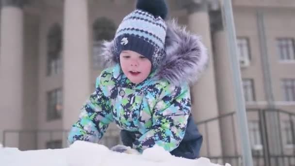 Uma criança pequena brinca em uma montanha nevada, joga neve e ri. Dia gelado ensolarado. Diversão e jogos ao ar livre . — Vídeo de Stock
