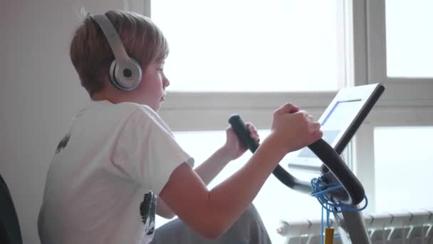 Adolescent dans un casque écoutant de la musique sur un vélo stationnaire exercisers.Gym et mode de vie sain — Video