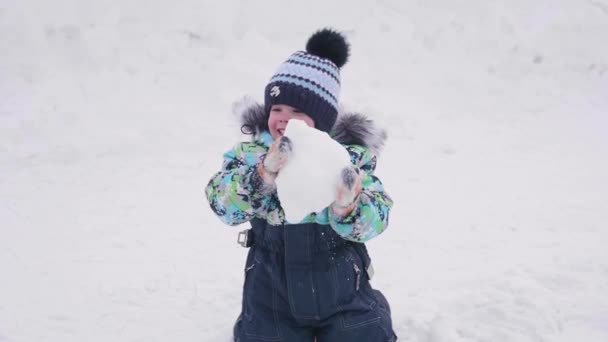 Ένα μικρό παιδί παίζει σε ένα χιονισμένο βουνό, ρίχνει χιόνι και γέλια. Ηλιόλουστη ημέρα ψυχρός. Διασκέδαση και παιχνίδια στο φρέσκο αέρα. — Αρχείο Βίντεο