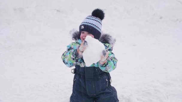 Un petit enfant joue sur une montagne enneigée, jette de la neige et rit. Journée ensoleillée et glacée. Fun et jeux dans l'air frais . — Video