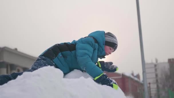 En tonåring ovanpå ett snöiga berg, kastar snö och skrattar. Solig frostig dag. Kul och spel i friska luften. — Stockvideo