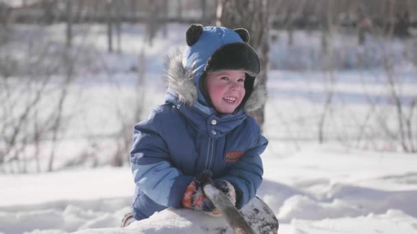 Uma criança pequena brinca no parque de inverno, ri e sorri. Dia gelado ensolarado. Diversão e jogos ao ar livre . — Vídeo de Stock