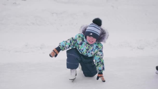 Первые шаги маленького ребенка на коньках. Мальчик на коньках упал и не мог подняться. Активный образ жизни — стоковое видео