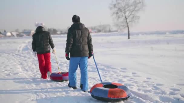 Zwei Personen fahren auf einem schneebedeckten Hügel auf einem Schlitten. ein Mann und ein Mädchen erklimmen den Gipfel des Berges. Spaziergänge an der frischen Luft — Stockvideo